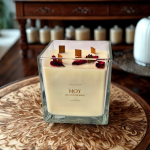 נר סויה ריחני עם עלי ורדים, מונח על שולחן עץ, מסביב נרות נוספים. מוצר ריחני איכותי לבית.