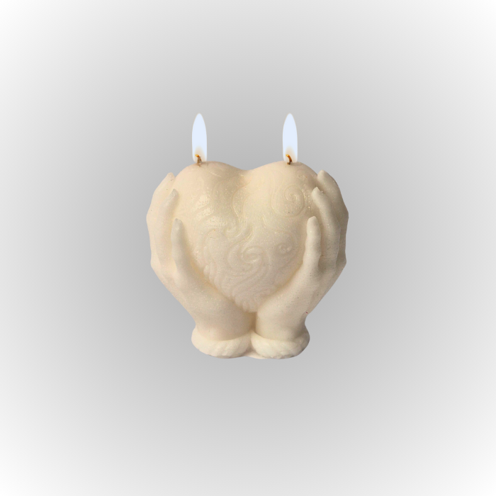 נר סויה ריחני בצורת לב, מוחזק על ידי ידיים, עם שני פתילים דולקים.