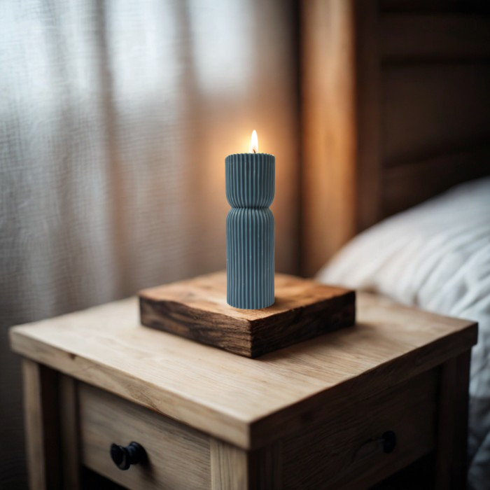 נר סויה ריחני בצבע כחול דלוק על שולחן עץ ליד מיטה, מוסיף אווירה חמימה לבית.